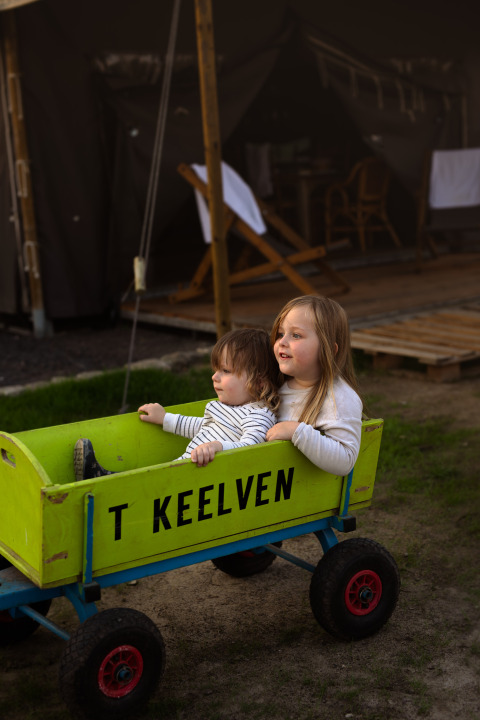 Deux enfants jouent dans une charrette verte marquée 'T KEELVEN' à Feather Down Het Keelven, Brabant-Septentrional.