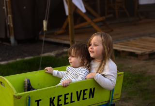 Deux enfants jouent dans une charrette verte marquée 'T KEELVEN' à Feather Down Het Keelven, Brabant-Septentrional.