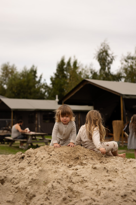 Børn leger på en sandbunke foran træhytter i Feather Down Het Keelven feriepark, Nord-Brabant, Holland.