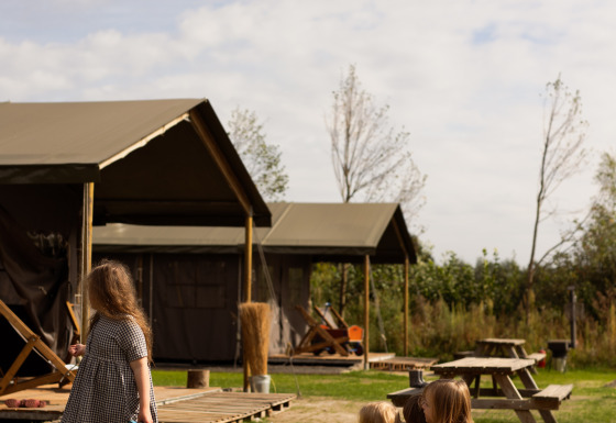 Ein Kind zieht einen Wagen mit zwei Kindern vor Zelten und Holzbänken im Feather Down Het Keelven Ferienpark.