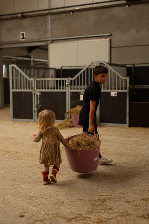 Zwei Kinder tragen einen Eimer mit Heu in einem Stall im Feather Down Het Keelven Ferienpark in Nordbrabant.