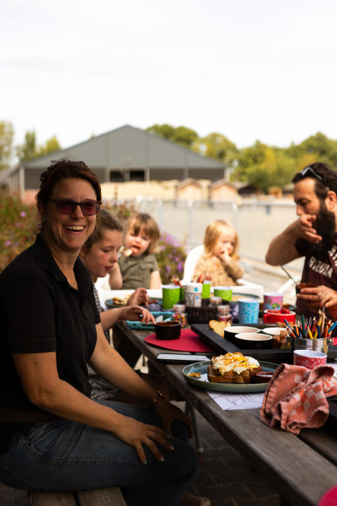 Famiglia che pranza all'aperto al tavolo del parco vacanze Feather Down Het Keelven in Brabante Settentrionale.