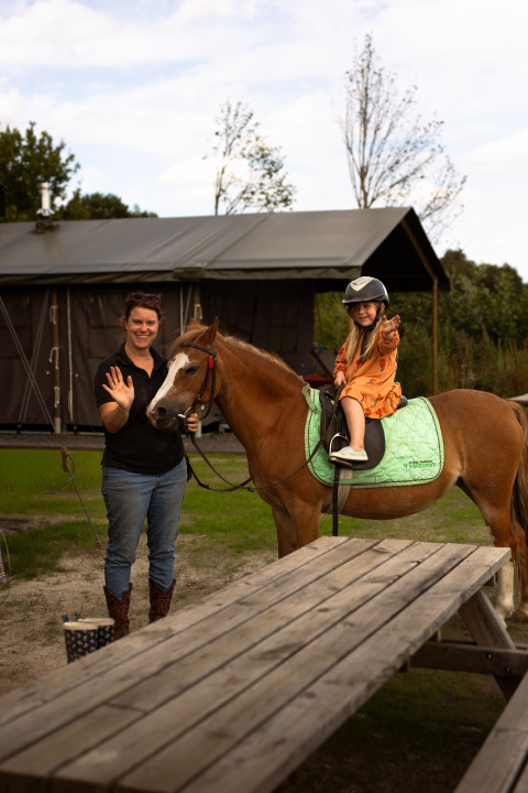 Femme et enfant à cheval à Someren, Brabant-Septentrional, Pays-Bas, saluant et souriant dehors.