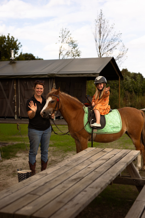 Frau und Kind auf einem Pferd in Someren, Nordbrabant, Niederlande, winken und lächeln im Freien.