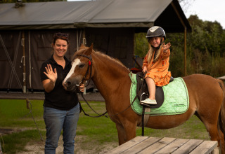 Frau und Kind auf einem Pferd in Someren, Nordbrabant, Niederlande, winken und lächeln im Freien.