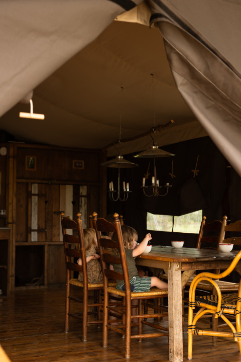 Twee kinderen zitten aan een houten tafel in een gezellige tent bij Feather Down Het Keelven, Noord-Brabant, Nederland.