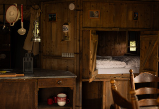 Cozy wooden cabin interior with bed in wall nook, kitchen area, and rustic decor at Feather Down Het Keelven.