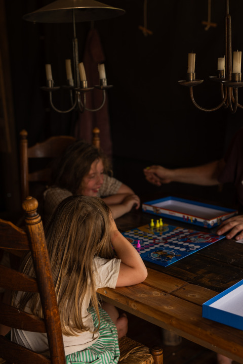 Kinder und Erwachsene spielen ein Brettspiel am Holztisch im Feather Down Het Keelven Ferienpark, Nordbrabant, Niederlande.