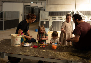 Family making crafts at a table in a barn at Feather Down Het Keelven holiday park, North-Brabant, Netherlands.
