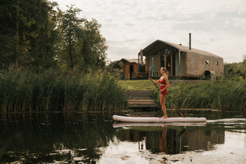 Mujer haciendo paddle surf frente a Wrap house con sauna y bañera en Resort de Parel, Países Bajos, naturaleza.