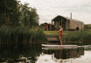 Femme en paddle devant Wrap house avec sauna et baignoire au Resort de Parel, Pays-Bas, proche de la nature.