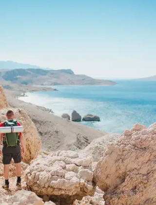 Due escursionisti con zaini camminano su terreni rocciosi vicino al mare blu a Povljana, Zadar, Croazia.