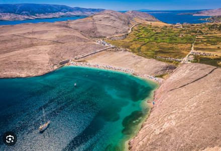 Vista aerea di Povljana, Croazia, con baia turchese, colline aride e campi verdi sullo sfondo.