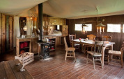 Intérieur d'une tente safari avec meubles en bois rustiques, table à manger et poêle à bois cosy.