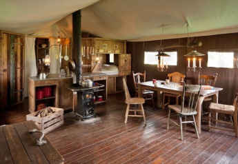 Intérieur d'une tente safari avec meubles en bois rustiques, table à manger et poêle à bois cosy.