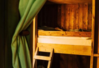 Intérieur de tente safari avec lit superposé en bois, rideau vert et lumière chaude et confortable.