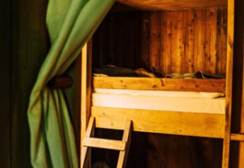 Interieur van een safaritent met houten stapelbed, groene gordijn en warme sfeerverlichting erbij.