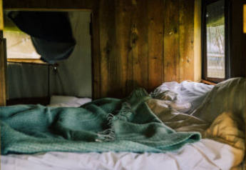 Lit douillet avec couverture verte dans une tente safari rustique, murs en bois et lumière naturelle.