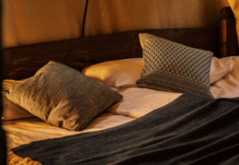 Lit douillet avec coussins et couverture à l'intérieur d'une tente safari, baigné de lumière chaude.