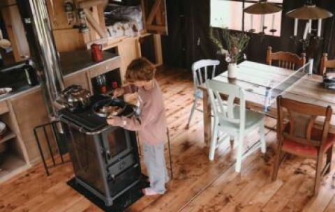 Un bambino cucina su una stufa in una cucina accogliente di tenda safari con tavolo e sedie di legno.
