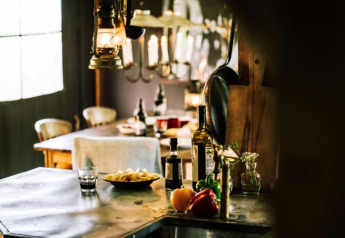 Cucina tipica in tenda safari con verdure fresche, bottiglia d'olio e lanterna su tavolo rustico.