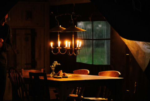Ein rustikaler Tisch in einem Safarizelt, beleuchtet von einer Kerzenlampe, mit Fenster dahinter.