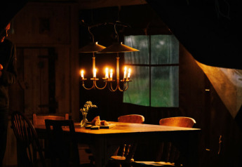 Ein rustikaler Tisch in einem Safarizelt, beleuchtet von einer Kerzenlampe, mit Fenster dahinter.