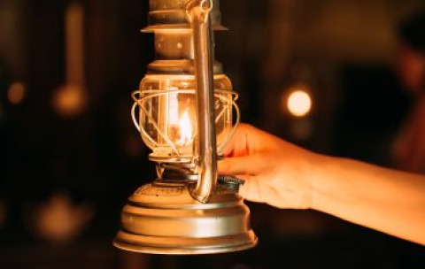 Hand mit einer brennenden Petroleumlampe im Safari-Zelt, stimmungsvolles Licht in warmer Atmosphäre.