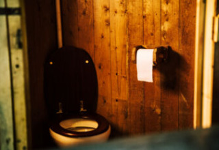 Eine einfache Toilette mit Holzverkleidung und Toilettenpapier, fotografiert im Safari-Zelt.