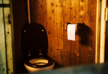 A basic toilet with wooden walls and a toilet roll, taken inside a safari tent with rustic decor.
