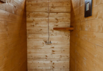Vista interna di una doccia in legno in una tenda safari con doccia a secchio e luce naturale.