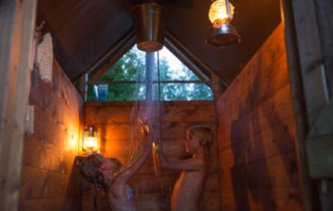 Kinder genießen eine warme private Dusche bei Laternenlicht in einem Safarizelt in Frankreich.
