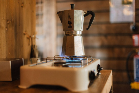 A moka pot brews coffee on a gas stove in a cozy wooden cabin, typical for a glamping accommodation.
