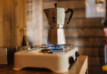 A moka pot brews coffee on a gas stove in a cozy wooden cabin, typical for a glamping accommodation.