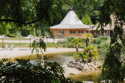 Alloggio glamping con casetta di legno, palme, spiaggia sabbiosa e laghetto immersi nel verde della natura.