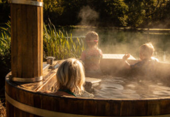 Kinderen ontspannen in een stomende buiten-hot tub bij een safaritent, omgeven door groene natuur.