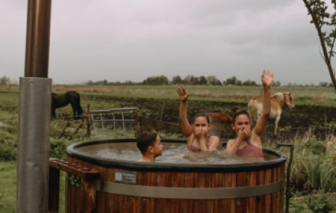 Drei Personen entspannen im holzernen Whirlpool vor einer Weide mit Pferden bei Feather Down Ecuries de Gapennes.