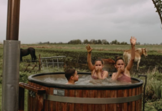 Drei Personen entspannen im holzernen Whirlpool vor einer Weide mit Pferden bei Feather Down Ecuries de Gapennes.