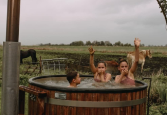 Trois personnes se détendent dans un bain nordique extérieur avec chevaux en arrière-plan à Feather Down, France.
