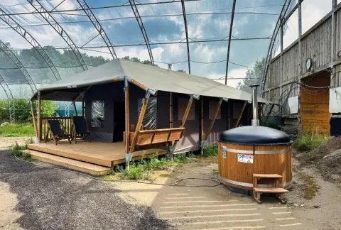 Tente safari avec terrasse couverte en bois, chaises longues et bain chaud privé sous une grande verrière.