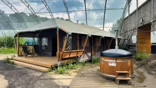 Safari-Zelt mit überdachter Terrasse, Liegestühlen und privatem Whirlpool, umgeben von Natur und Struktur.