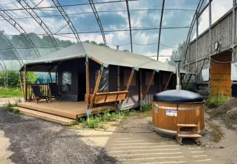Tenda safari con veranda coperta in legno, lettini e vasca idromassaggio privata sotto una grande struttura.