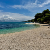 Kieselstrand und türkisblaues Meer bei Baška, Kroatien, mit Kiefernwald und malerischen Wolken.