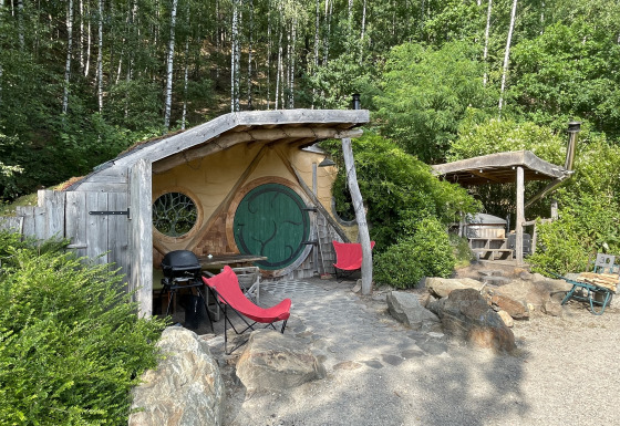 Lille Hobbit-hus med rund dør og to røde stole, omgivet af skov i Limburg, Belgien.