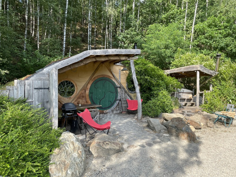 Kleine hobbitwoning met ronde deur en rode stoelen in het bosrijke Limburg, België.