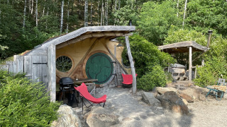 Kleine hobbitwoning met ronde deur en rode stoelen in het bosrijke Limburg, België.
