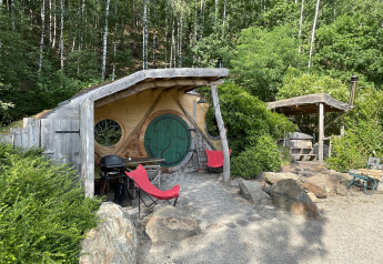 Lille Hobbit-hus med rund dør og to røde stole, omgivet af skov i Limburg, Belgien.