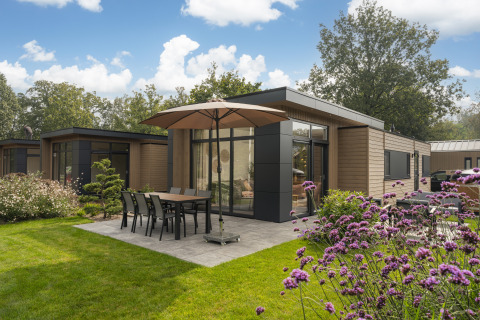 Alloggio glamping moderno con patio, tavolo da giardino e ombrellone, immerso nel verde.