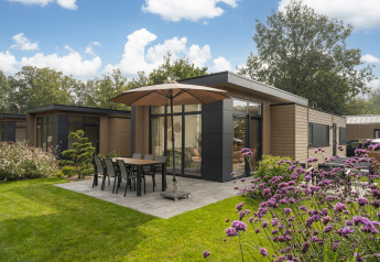 Hébergement glamping moderne avec terrasse, mobilier de jardin et parasol, entouré de verdure.