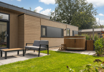 Alojamiento de glamping moderno con fachada de madera, jacuzzi exterior y área de descanso en césped.